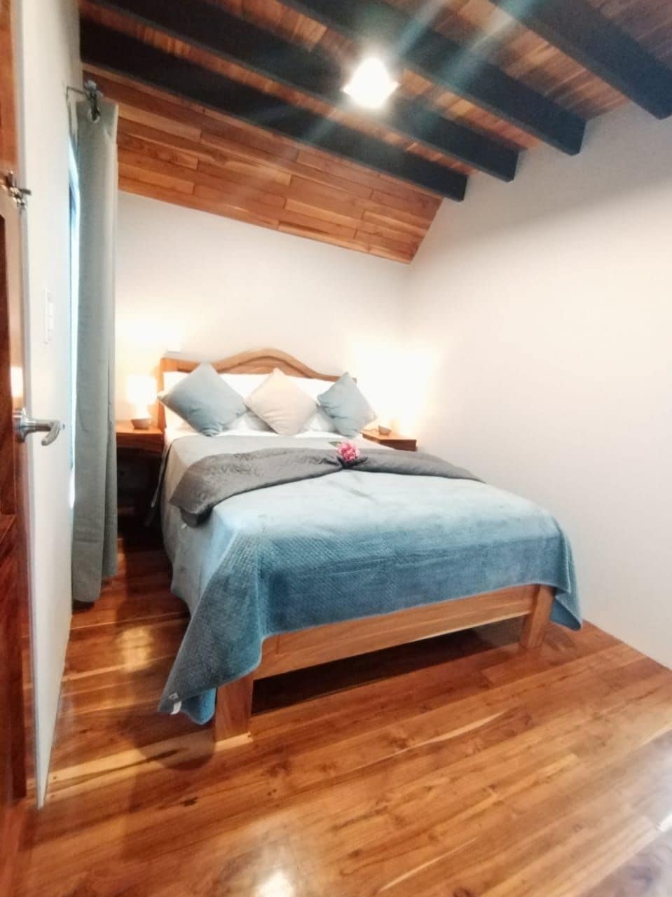 Quarto com cama de madeira, mesa de cabeceira e teto com vigas aparentes.