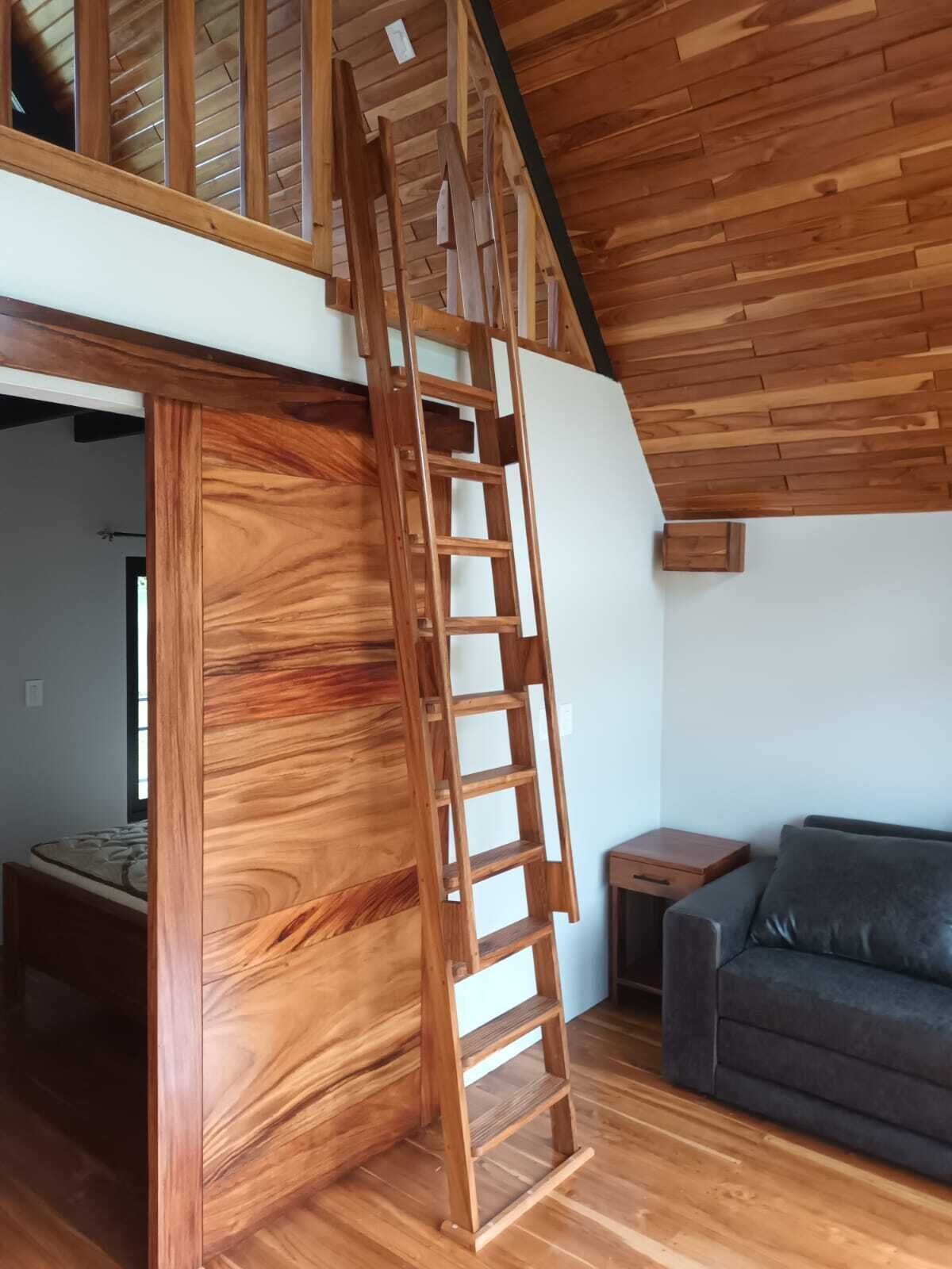 A wooden staircase leading to an upper level in a room with a wooden floor, a gray sofa, and a small wooden table.