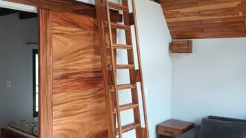 A wooden staircase leading to an upper level in a room with a wooden floor, a gray sofa, and a small wooden table.
