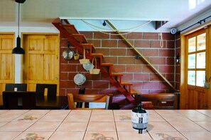 Un coin repas avec une table carrelée, des chaises en bois, un escalier en bois et un mur en briques.