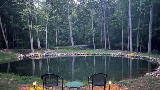 Un étang entouré d’arbres, avec deux chaises et une table au premier plan.