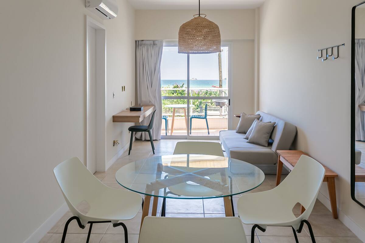 Ein modernes Wohnzimmer mit Glastisch, weißen Stühlen, einer Couch und einem Balkon mit Meerblick.