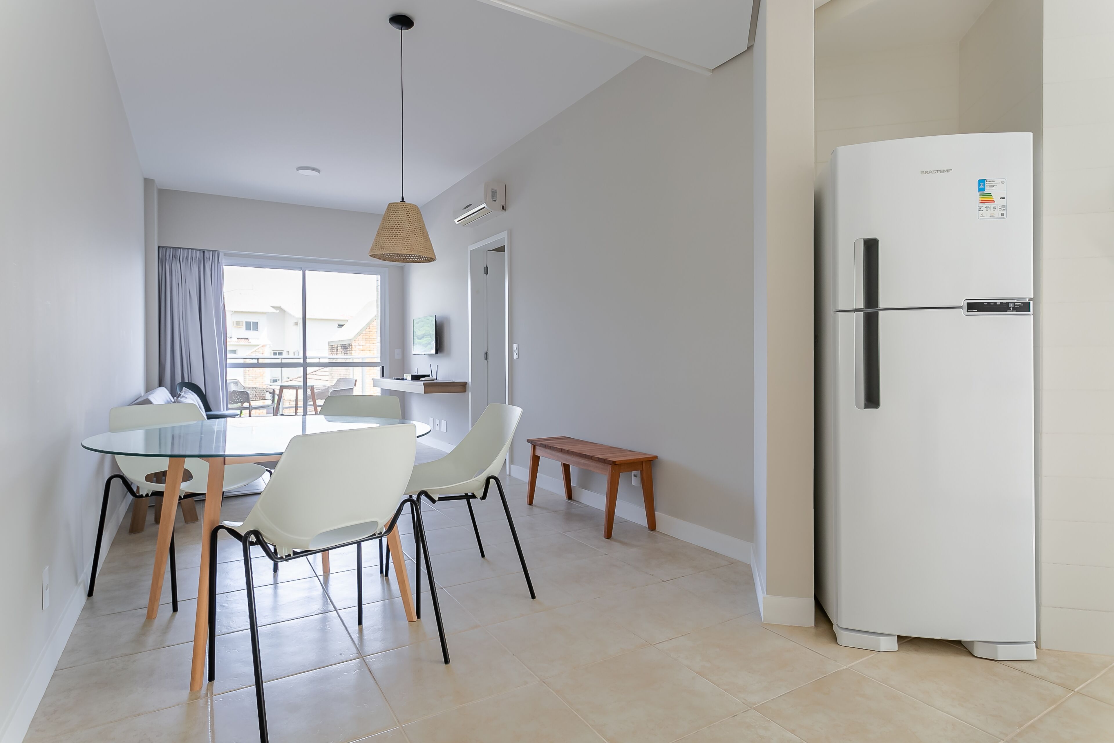 A modern kitchen with a white refrigerator, a dining table with chairs, and a hanging light fixture.