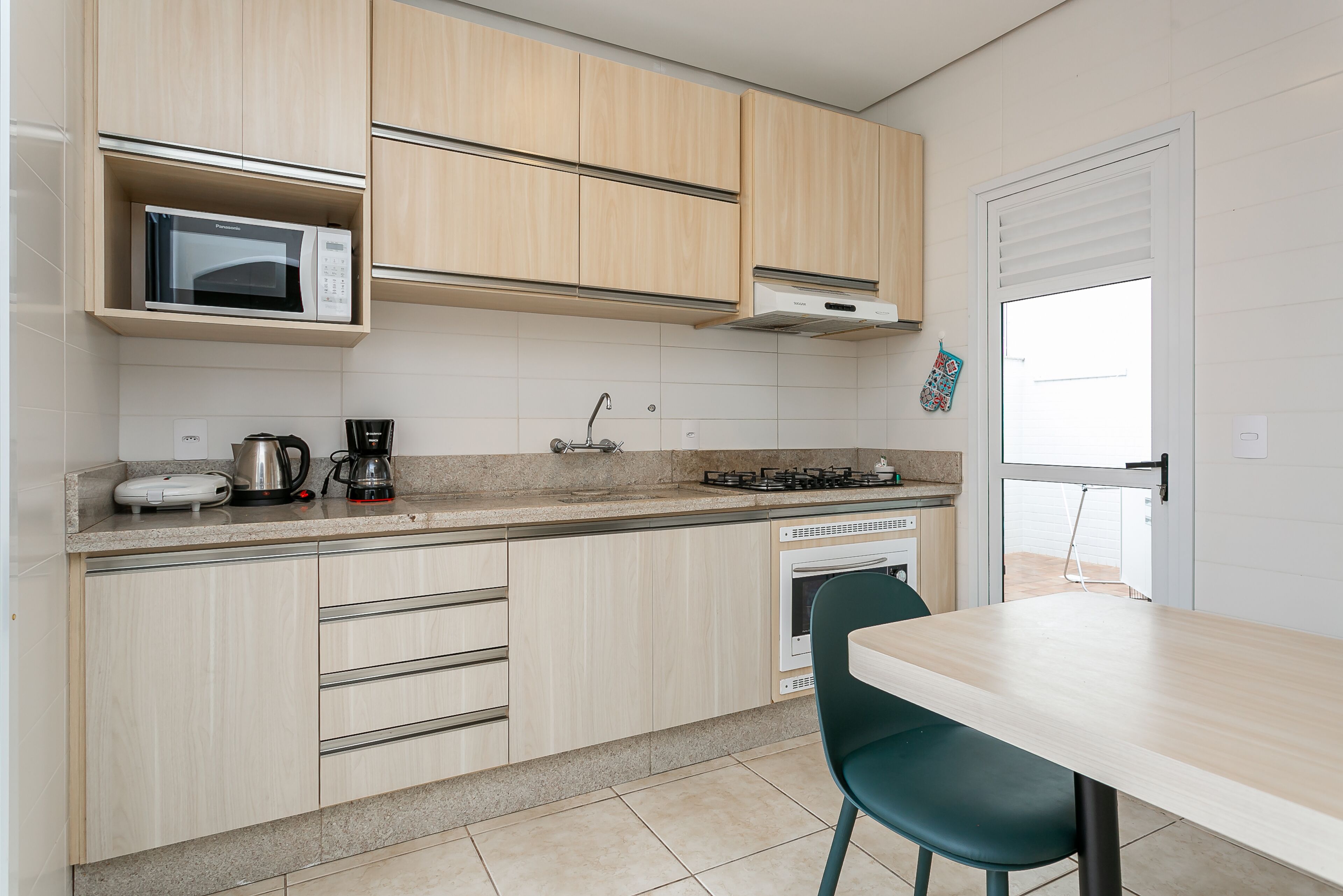 Une cuisine moderne avec des meubles de couleur bois clair, un four à micro-ondes, une machine à café et une cuisinière à gaz.