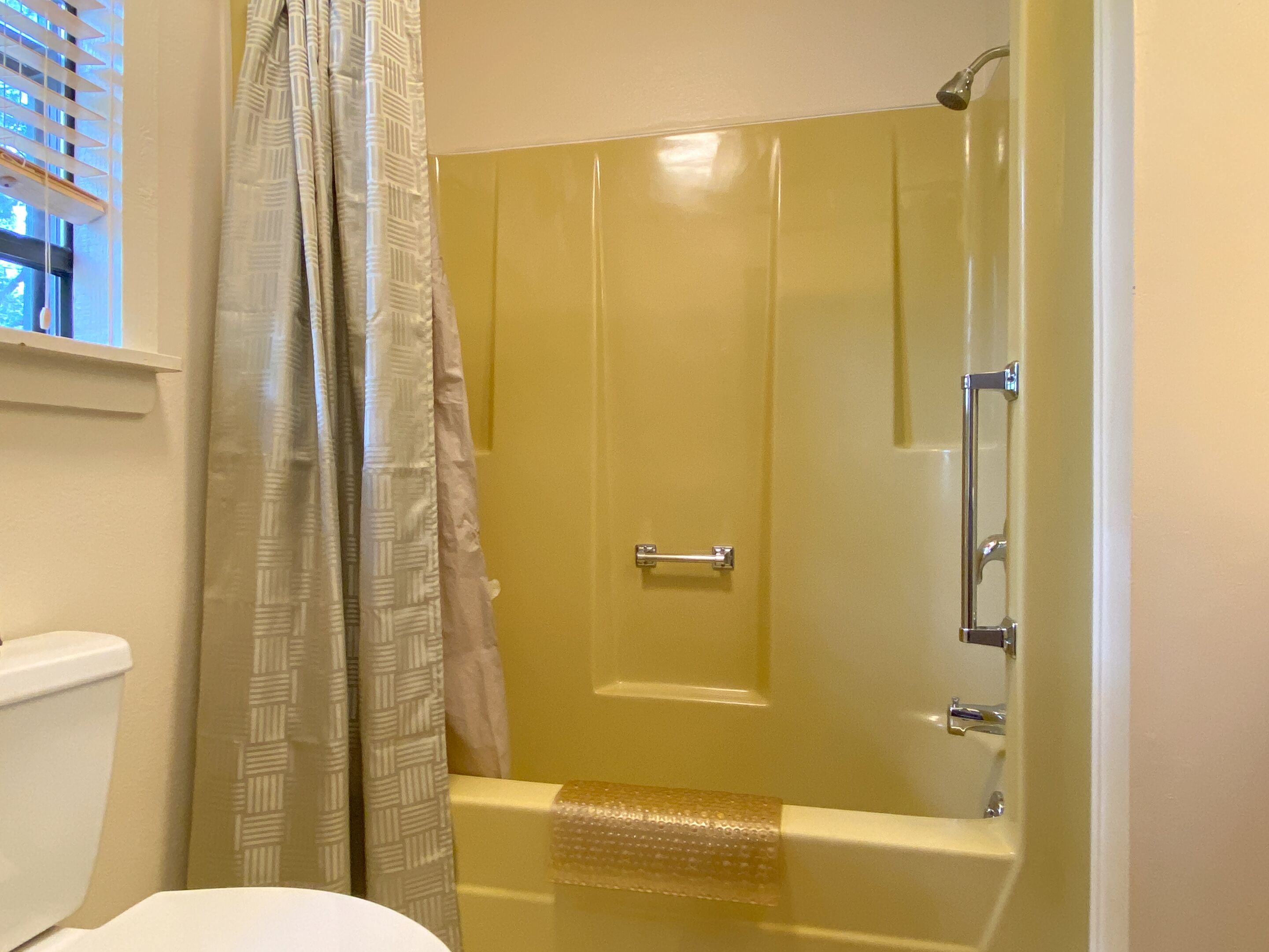 A bathroom with a shower enclosure, a toilet, and a window with blinds.