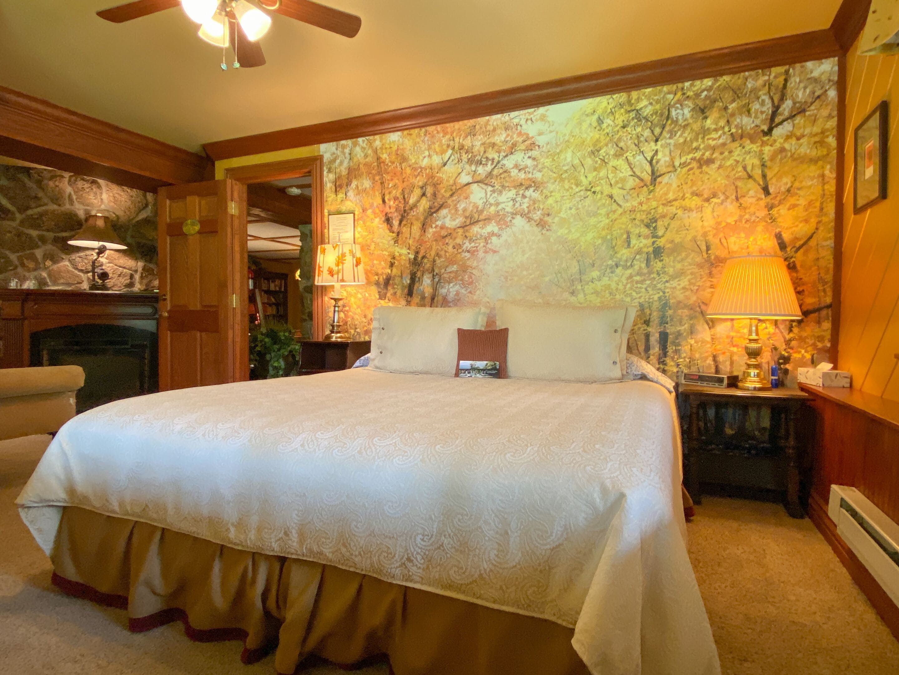 A bedroom with a large bed, a fireplace, and a forest mural on the wall.