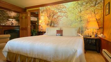 A bedroom with a large bed, a fireplace, and a forest mural on the wall.