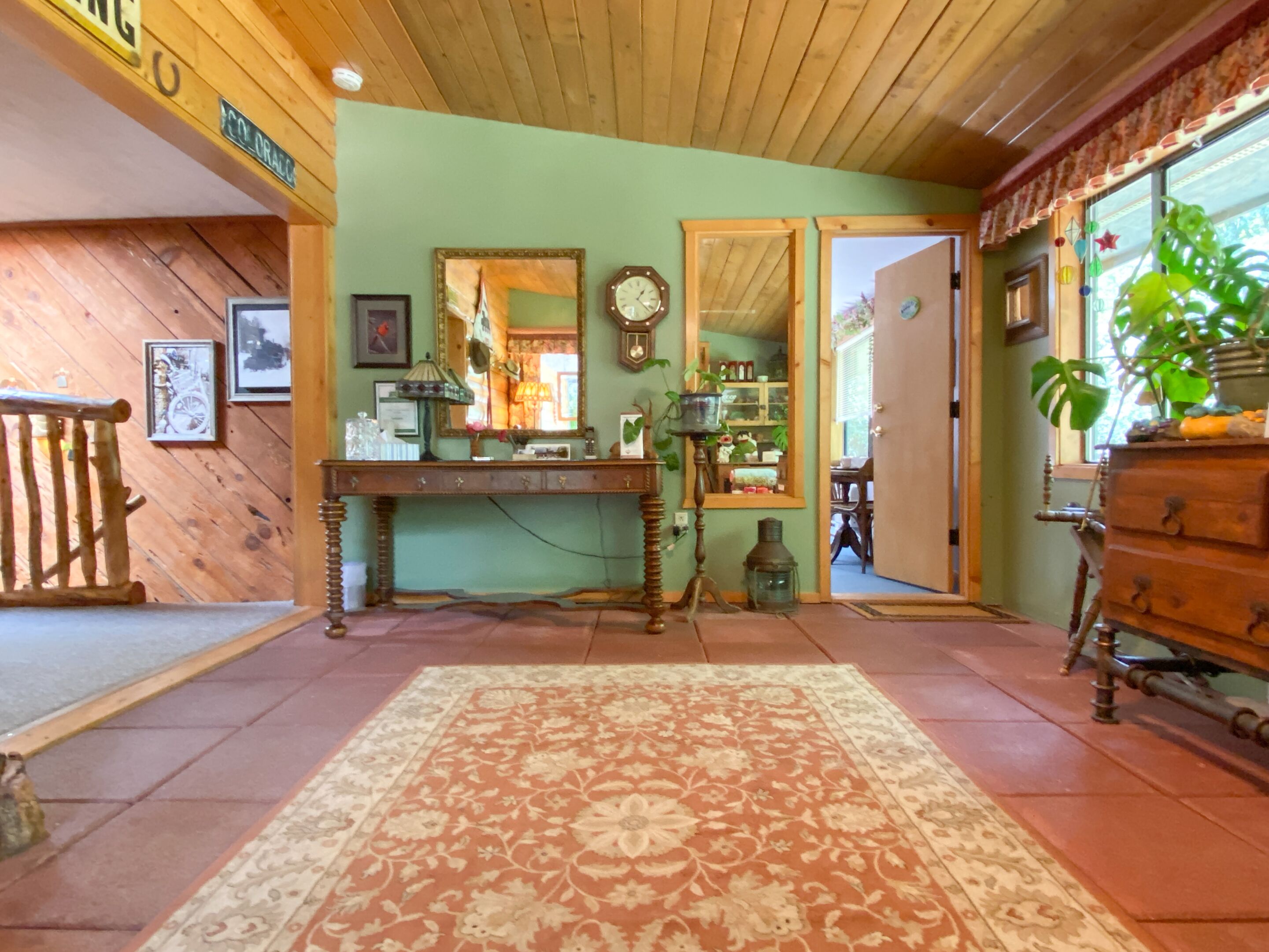 A cozy room with a wooden ceiling, a large mirror, a vintage clock, and a rustic wooden desk.