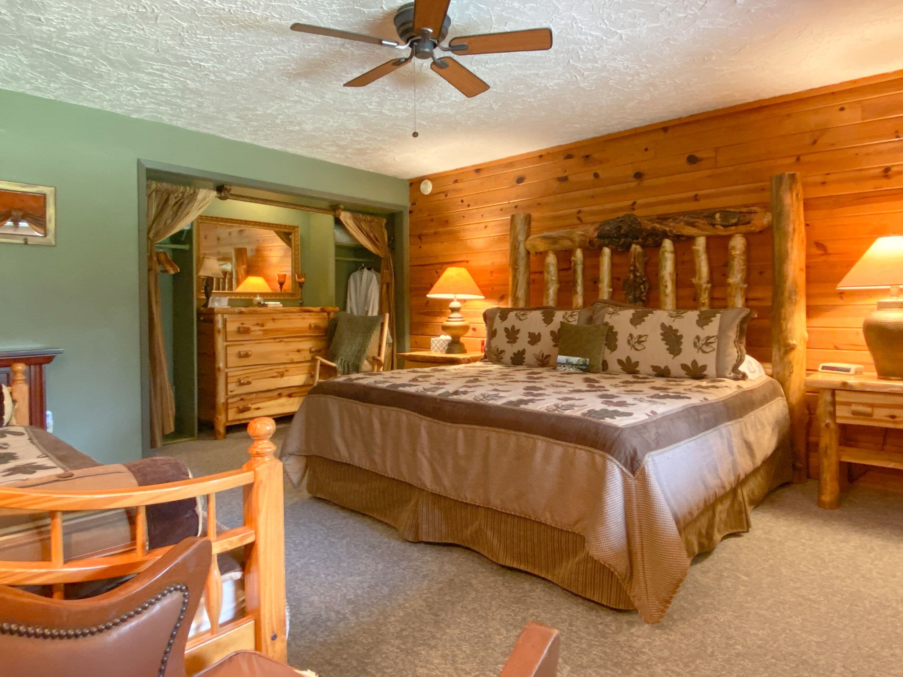 Une chambre chaleureuse avec une tête de lit en bois, un lit recouvert d’une literie à motifs floraux, une commode en bois et un ventilateur de plafond.