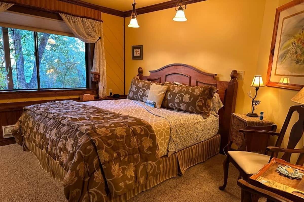 A bedroom with a large bed, a wooden headboard, a nightstand, a chair, and a window with curtains.