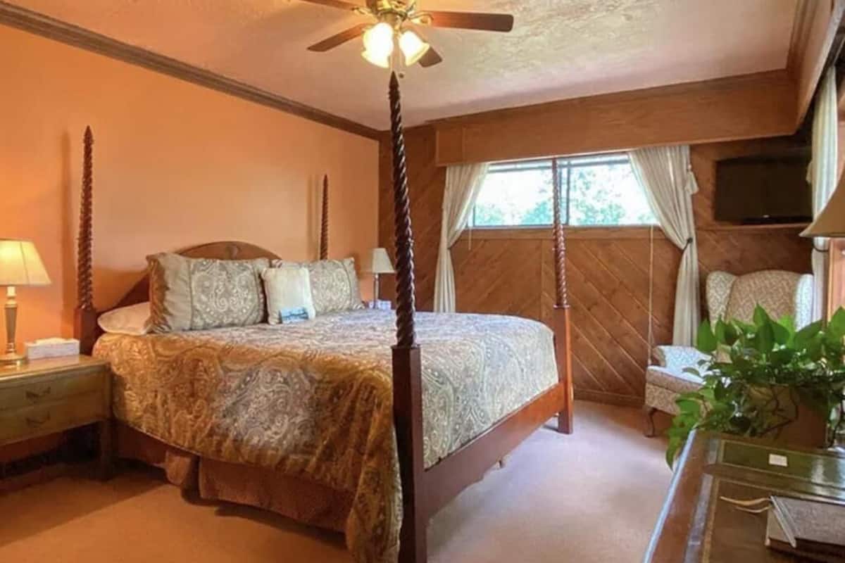 A four-poster bed with a wooden headboard, a ceiling fan, and a window with curtains.