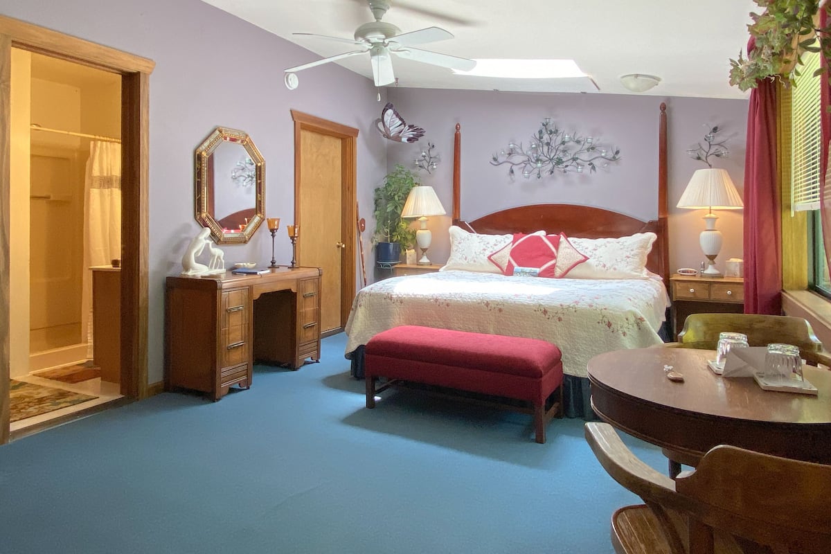 A bedroom with a bed, a desk, a chair, a ceiling fan, and a window with curtains.