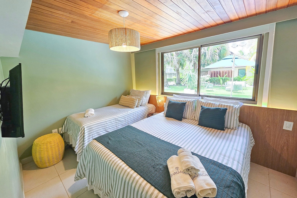 A hotel room with two beds, a window with a view of the outdoors, a ceiling fan, and a television.