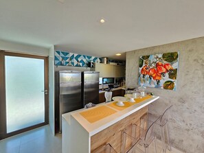 A modern kitchen with stainless steel appliances, a central island, and a decorative painting. - Lindos Bangalôs - Carneiros Beach Resort (Tamandaré)