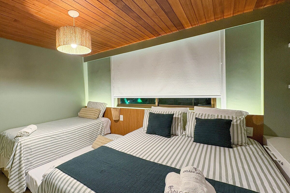 A room with two beds, a wooden ceiling, a hanging light fixture, and a window with blinds.