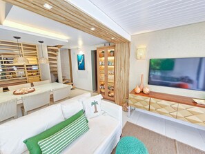 A modern living room with a sofa, TV, and a dining area with a table and chairs. - Lindos Bangalôs - Carneiros Beach Resort (Tamandaré)