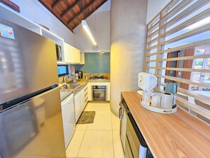 A compact kitchen with stainless steel appliances, a built-in oven, and a window with a wooden blind. - Lindos Bangalôs - Carneiros Beach Resort (Tamandaré)