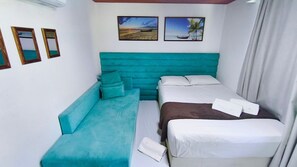A room with a teal sofa, a bed with white bedding, and two framed pictures on the wall. - Lindos Bangalôs - Carneiros Beach Resort (Tamandaré)