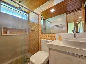A modern bathroom with a glass shower enclosure, a toilet, a sink with a mirror, and a tiled backsplash. - Lindos Bangalôs - Carneiros Beach Resort (Tamandaré)