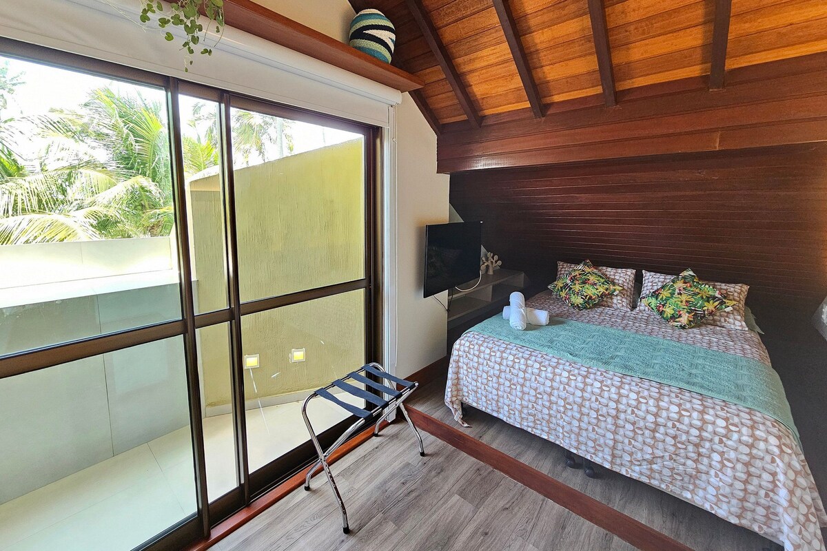 A room with a bed, a TV, a window, and a plant.