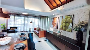 A modern living room with a dining area, featuring a sofa, a coffee table, and a dining table set with plates and glasses. - Lindos Bangalôs - Carneiros Beach Resort (Tamandaré)