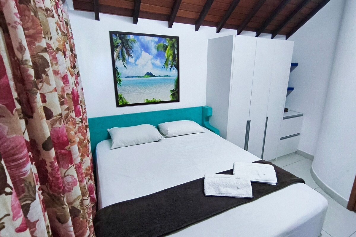 A bedroom with a bed, a painting of a beach, and a wardrobe.