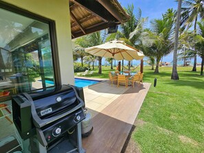 A patio with a grill, outdoor furniture, and a view of the pool and ocean. - Lindos Bangalôs - Carneiros Beach Resort (Tamandaré)