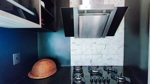 A modern kitchen with a stainless steel range hood, a gas stove, and a woven basket. - Lindos Bangalôs - Carneiros Beach Resort (Tamandaré)