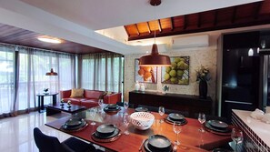 A dining area with a wooden table set for four, a red sofa, and a large window with curtains. - Lindos Bangalôs - Carneiros Beach Resort (Tamandaré)