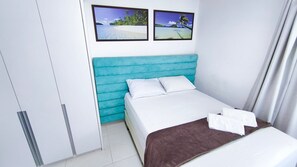 A hotel room with a bed, a blue headboard, a brown throw blanket, and two framed pictures on the wall. - Lindos Bangalôs - Carneiros Beach Resort (Tamandaré)