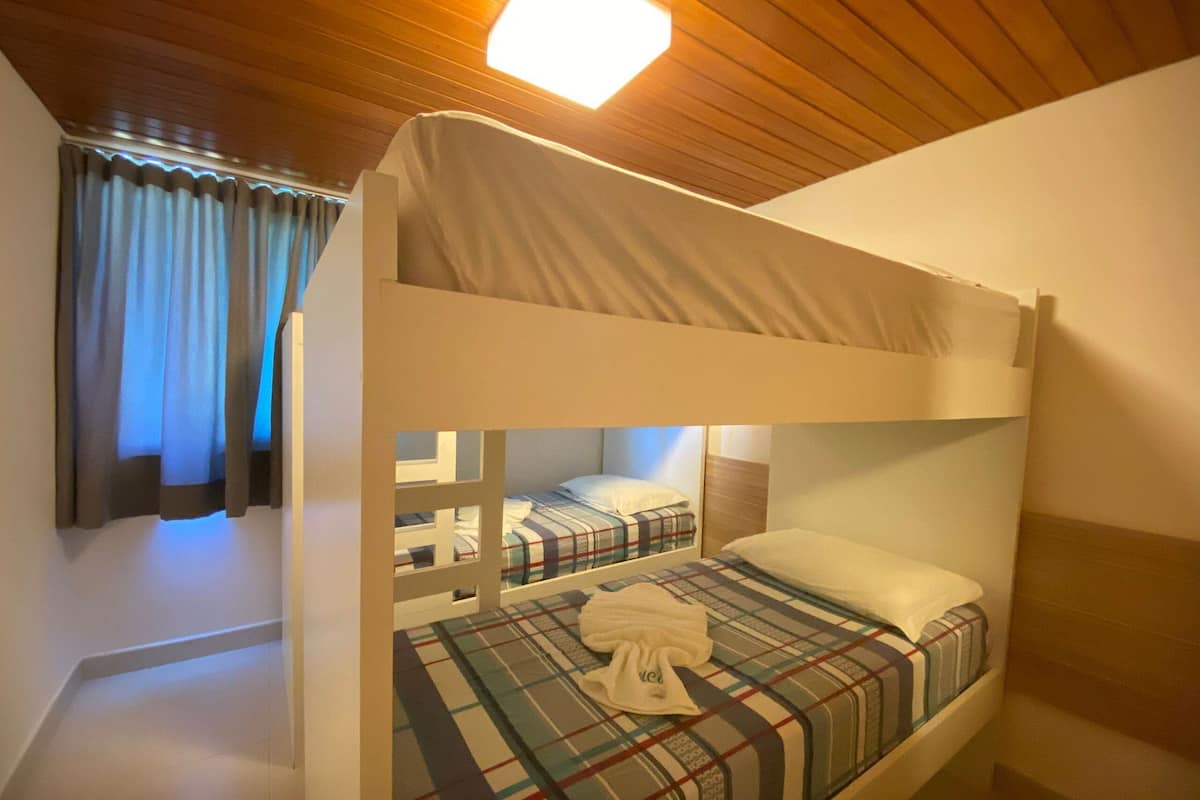 Ein Schlafraum mit Etagenbetten, Holzbalkendecke, karierter Bettdecke und einem weißen Handtuch auf dem Bett.