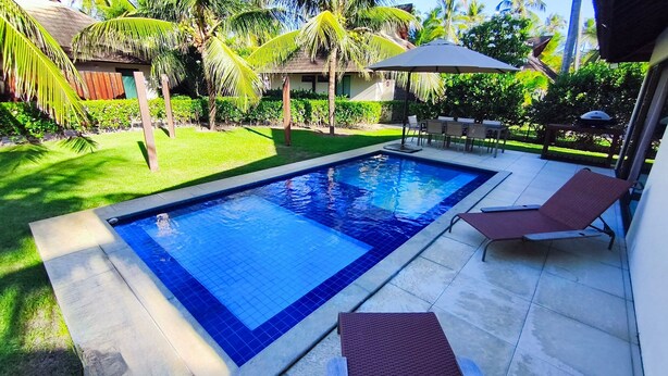A rectangular swimming pool with a tiled edge, surrounded by a patio area with chairs and a table. - Lindos Bangalôs - Carneiros Beach Resort (Tamandaré)