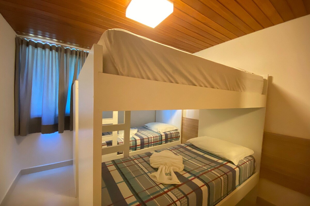 A bunk bed room with a wooden ceiling, a plaid bedspread, and a white towel on the bed.