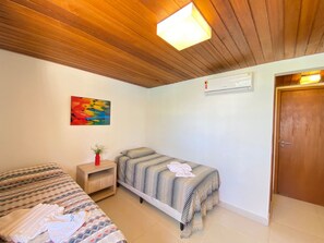 A room with two beds, a wooden ceiling, a wall-mounted air conditioner, and a colorful abstract painting. - Lindos Bangalôs - Carneiros Beach Resort (Tamandaré)