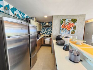A modern kitchen with stainless steel appliances, a tiled backsplash, and a painting of flowers on the wall. - Lindos Bangalôs - Carneiros Beach Resort (Tamandaré)