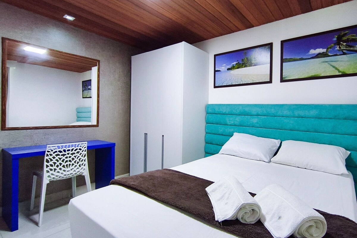 A bedroom with a bed, a desk, and two wall-mounted pictures.