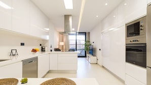 Una cocina moderna con armarios blancos, una isla central y electrodomésticos integrados, incluyendo un microondas y un horno.