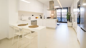 Una cocina moderna con armarios blancos, una isla central con taburetes, lavavajillas integrado y un amplio ventanal con vistas a la ciudad.