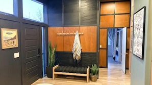 Een modern interieur met een donkere muur, een houten bank, planten in potten en een gang naar een andere kamer.