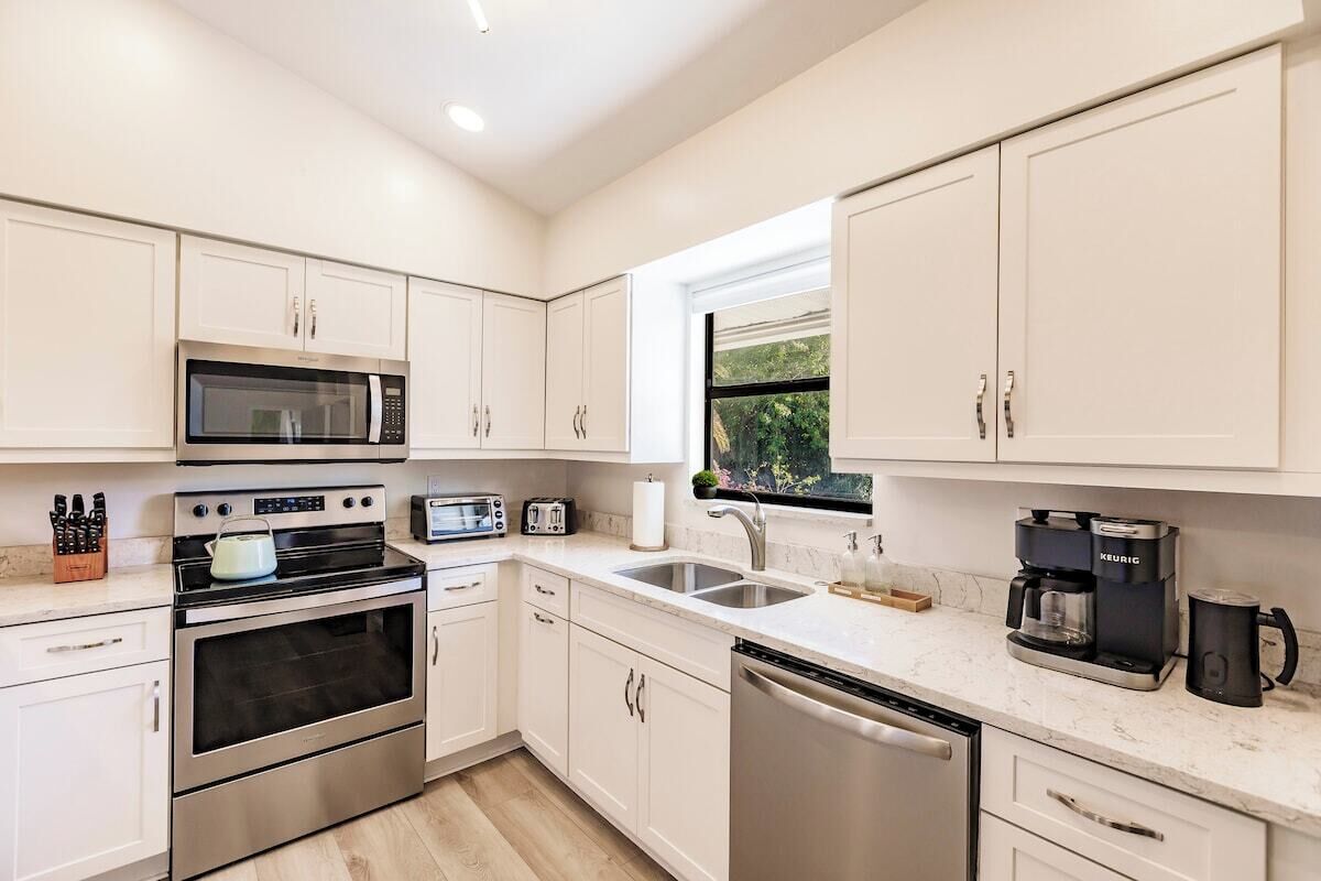 Una cocina moderna con electrodomésticos de acero inoxidable, armarios blancos y un ventanal que proporciona luz natural.