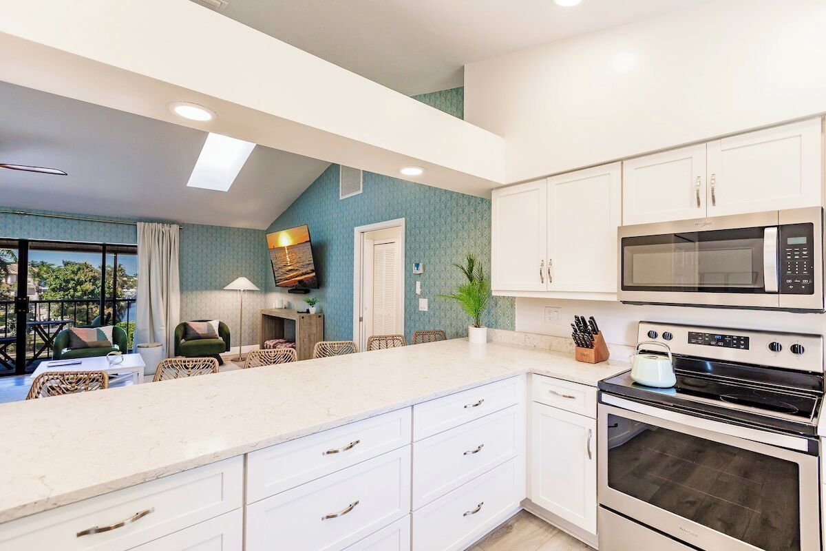 A modern kitchen with white cabinetry, a large island, and built-in appliances including a microwave and oven.
