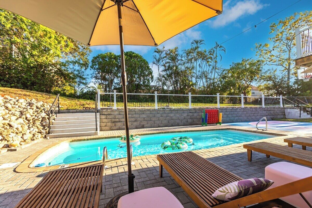 A swimming pool with lounge chairs and an umbrella, surrounded by a stone wall and greenery.
