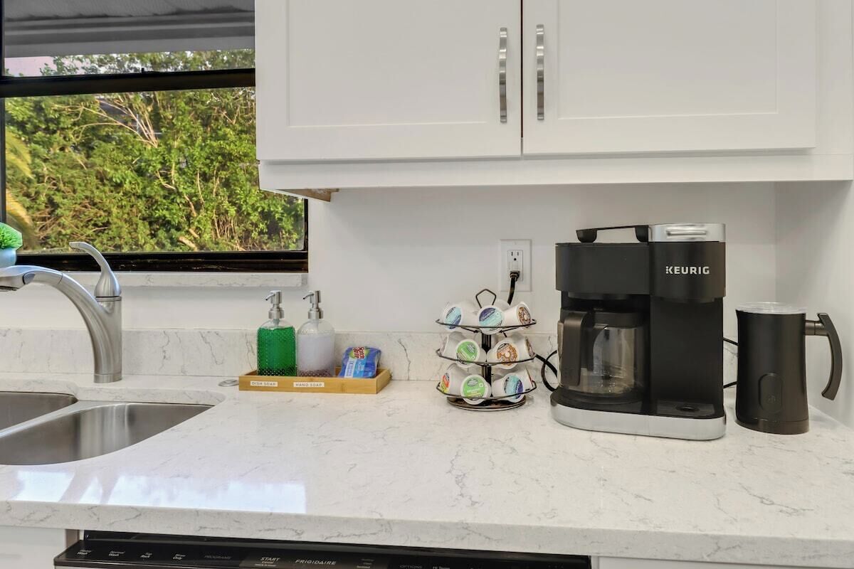 Una cocina con cafetera, escurreplatos y dispensador de jabón para lavar platos.