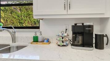 Una cocina con cafetera, escurreplatos y dispensador de jabón para lavar platos.
