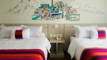 Quarto de hotel com duas camas, cada uma com roupa de cama branca e cobertores listrados coloridos. Pequena mesa de cabeceira com telefone e interruptor de luz na parede. Acima das camas, um mural colorido retrata uma paisagem de montanhas com edifícios e um teleférico.