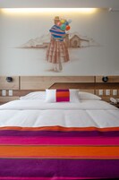 Habitación de hotel con cama, un mural en la pared y cabecera de madera.