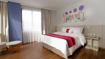 A modern hotel room with a large bed, a bedside table, a small round table, and a large window with curtains.