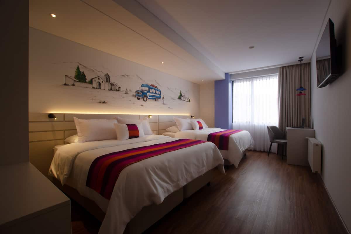 A hotel room with two beds, a desk, a chair, a TV, and a mural on the wall.