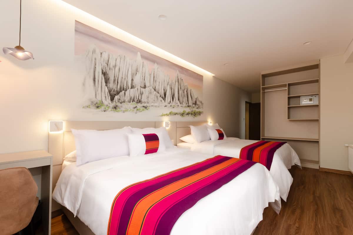 A hotel room with two beds, a desk, and a wall-mounted shelf.