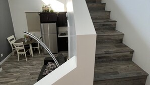 A modern interior with a staircase leading to a lower level, a dining area with a table and chairs, and a kitchen area with a refrigerator and cabinets.